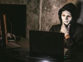 Computerhacker - Mann im Kapuzenshirt mit Maske, der Daten vom Laptop stiehlt foto