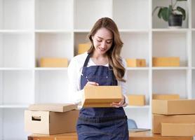 Porträt einer asiatischen jungen Frau, die zu Hause mit einer Kiste am Arbeitsplatz arbeitet. Start-up-Kleinunternehmer, Kleinunternehmer-KMU oder freiberufliches Online- und Lieferkonzept. foto