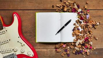 Draufsicht-Arbeitsbereich mit Notizbuch, Stift, E-Gitarre und getrockneten Blumen auf Holztischhintergrund. foto
