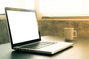 laptop mit weißem leerem bildschirm, weißer tasse kaffee auf dem schreibtisch, vintage-ton foto