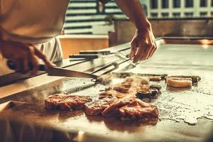 Nahaufnahme der Hände Küchenchef kocht Rindersteak und Gemüse auf heißer Pfanne, japanisches Essen foto