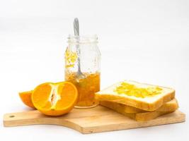 frische Orange mit Orangenmarmelade im Glas und Brot auf Holztablett auf weißem Hintergrund. foto