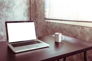 laptop mit weißem leerem bildschirm, weißer tasse kaffee auf dem schreibtisch, vintage-ton foto