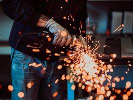 schwerindustrie-fabrikinnenraum mit industriearbeiter, der winkelschleifer verwendet und ein metallrohr schneidet. Auftragnehmer in der Herstellung von Metallstrukturen für Sicherheitsuniformen und Schutzhelme. foto