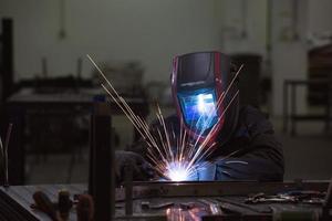 professioneller Schweißer aus der Schwerindustrie, der in der Fabrik arbeitet, einen Helm trägt und mit dem Schweißen beginnt. selektiver Fokus