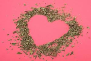 Zerkleinerte Marihuana-Herzform auf einem rosafarbenen Hintergrund Feiertagsvalentinstag für Cannabisliebhaber foto