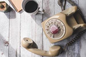 Draufsicht des alten Telefons mit Kaffeetasse, Notizbuch und Kaktus auf weißem Holztischhintergrund. foto