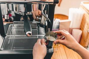 Der Barista verwendet eine Kaffeemaschine, um frische Milch in den Schaum zu rühren, um einen Cappuccino oder Latte in einem Café zuzubereiten foto