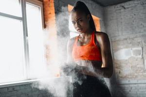 konzentrierte afrikanische frau, die vor dem training im fitnessstudio die hände mit talkumpuder vorbereitet foto