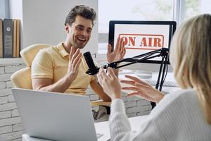 glücklicher junger Mann gestikuliert, während er ein Podcast-Interview mit einem Gast im Studio aufnimmt foto