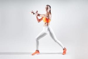 Selbstbewusste junge Frau in Sportkleidung, die Dehnübungen vor weißem Hintergrund macht foto