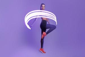 Selbstbewusste junge Frau in Sportkleidung, die sich vor violettem Hintergrund bewegt foto