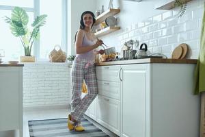 in voller Länge von einer glücklichen jungen Frau mit Kopfhörern, die Musik beim Kochen in der Küche genießt foto