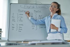 glückliche junge frau, die whiteboard zeigt, während sie im klassenzimmer steht foto