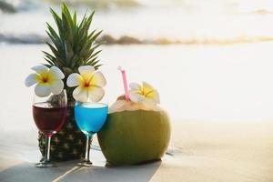 Cocktailgläser mit Kokosnuss und Ananas am sauberen Sandstrand - Obst und Getränke am Meeresstrand im Hintergrund foto