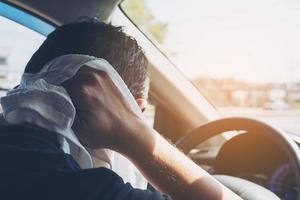 müder Mann, der sein Gesicht mit einem weißen kalten Erfrischungstuch abwischt, während er ein Auto fährt - lange Fahrt mit müdem Konzept foto