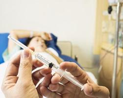 Arzt, der die Spritze in der Hand hält, bereit für die Injektion mit einem Patientenhintergrund im Krankenhaus foto