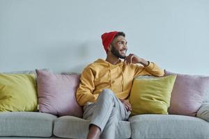 Schöner afrikanischer Mann, der nachdenklich aussieht, während er auf der Couch sitzt foto