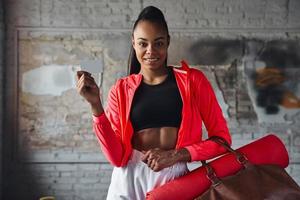glückliche junge afrikanerin in sportkleidung mit fitnesskarte foto