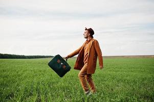 Stilvoller Mann mit Brille, brauner Jacke und Hut mit Tasche auf der grünen Wiese. foto