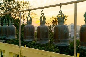 metallische Glocken hängen in einer Reihe draußen im thailändischen buddhistischen Tempel foto