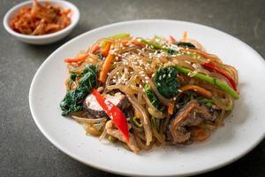 Japchae oder gebratene koreanische Fadennudeln mit Gemüse und Schweinefleisch, garniert mit weißem Sesam foto