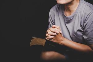 Nahaufnahme der Hand der christlichen Frau auf der Heiligen Bibel sind Gebet und Anbetung für Gott sei Dank in der Kirche mit schwarzem Hintergrund, Konzept für Glauben, Spiritualität und Religion foto