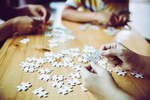 Hände einer Person, kleines Kind und Elternteil, die zu Hause zusammen auf einem Holztisch ein Puzzlespiel spielen, Konzept für die Freizeit mit der Familie, Spiel mit der Entwicklung, Bildung und Spaß der Kinder.