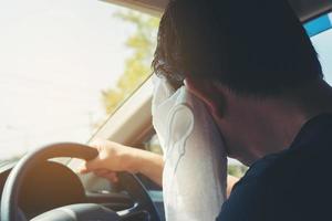 müder Mann, der sein Gesicht mit einem weißen kalten Erfrischungstuch abwischt, während er ein Auto fährt - lange Fahrt mit müdem Konzept foto
