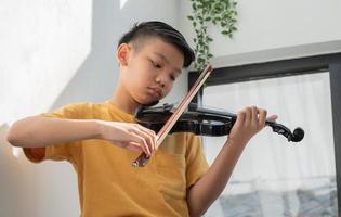 ein kleines asiatisches kind spielt und übt geigenmusiksaiteninstrument gegen zu hause, konzept der musikalischen ausbildung, inspiration, jugendlicher kunstschüler. foto