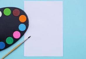 Kunstpalette mit Farbe, Pinsel und Papier auf blauem Hintergrund. foto