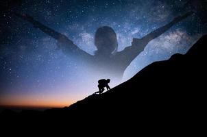 Ein junger Tourist mit Rucksack klettert nachts allein auf eine Klippe mit Stern, Milchstraße über dem Himmel. er musste sich anstrengen, um den ganzen Weg bis zur Spitze des Berges zu erklimmen, und es musste ihm gelingen. foto