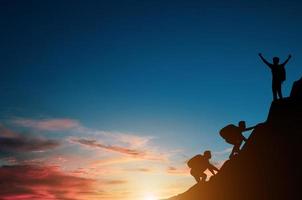 Silhouettengruppe von Touristen mit Rucksack klettert bei Sonnenaufgang allein auf eine Klippe. er musste sich anstrengen, um den ganzen Weg bis zur Spitze des Berges zu erklimmen, und es musste ihm gelingen. foto