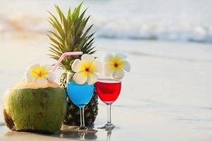 Cocktailgläser mit Kokosnuss und Ananas am sauberen Sandstrand - Obst und Getränke am Meeresstrand im Hintergrund foto