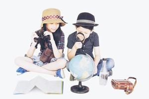 asiatische Jungen und Mädchen, die Reisende studieren, bereiten sich auf die Weltkarte vor, isoliert auf weißem Hintergrund foto