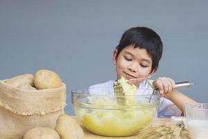7-jähriger Junge, der glücklich Kartoffelpüree macht foto