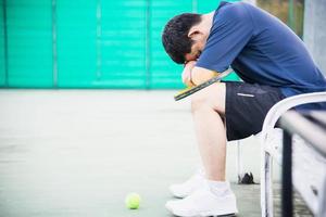 Trauriger Tennisspieler, der auf dem Platz sitzt, nachdem er ein Match verloren hat - Menschen im Sporttennis-Spielkonzept foto