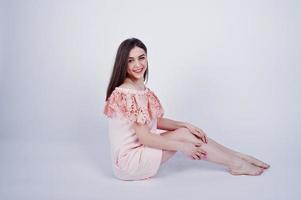 Porträt einer modischen Frau in rosafarbenem Kleid, die im Studio auf dem Boden sitzt und posiert. foto