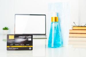 Kreditkartenvorderseite des Laptopbildschirms mit Händedesinfektionsmittel und OP-Maske foto