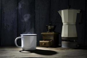 Emaillierte Tasse Kaffee mit Rauch. kaffeeset mit moka-kanne und mühle auf dem alten holzboden. Weicher Fokus.