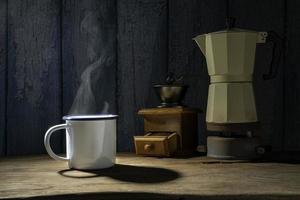 Emaillierte Tasse Kaffee mit Rauch. kaffeeset mit moka-kanne und mühle auf dem alten holzboden. Weicher Fokus.