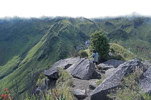 Junge Kletterer auf felsigen Berggipfeln mit Blick auf die grüne Bergkette, die an einem Sommertag mit Wolken auf ihrem Gipfel bedeckt ist. Landschaft mit Wanderern, wolkenverhangene Berge nach oben foto