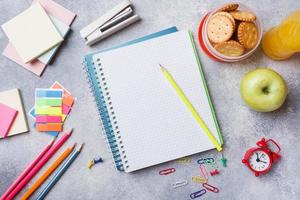 schulbedarf und frühstückscracker, orangensaft und frischer apfel auf dem grauen tisch mit kopierraum. Konzept Schule. foto