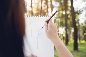 Entspannen Sie Frau, die Aquarellkunstwerk in der grünen Gartenwaldnatur malt - Menschen mit kreativer Kunst in der Natur Stressabbau und Meditationskonzept foto