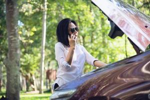 asiatische frau, die handwerker oder versicherungspersonal anruft, um ein automotorproblem auf einer lokalen straße zu beheben - menschen mit autoproblemen transportkonzept foto