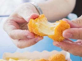 Die Hand hält einen Stretch-Käseball, der bereit ist, mit weich fokussierten Pommes Frites auf blauem Tischhintergrund gegessen zu werden foto