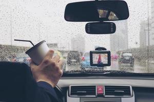 Mann, der Auto mit Navigator fährt und an regnerischen Tagen eine Kaffeetasse hält