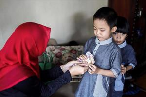 indonesische Volkstradition während der Eid Mubarak-Feier des Verteilens von Geld oder Thr genannt. asiatische muslimische frau gibt süßem jungen der familie während idul fitri geld. foto