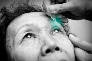 Nahaufnahme der älteren Frau tropft Augentropfen in ihre Augen mit grünem Fleck auf dem Tropfen. Schwarz-Weiß-Ton. Behandlung von Augenkrankheiten. Gesundheitskonzept foto