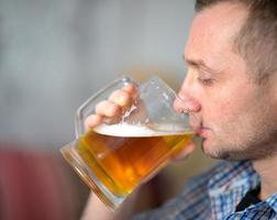 Mann trinkt frisches kaltes alkoholisches Bier aus einem großen Becher foto